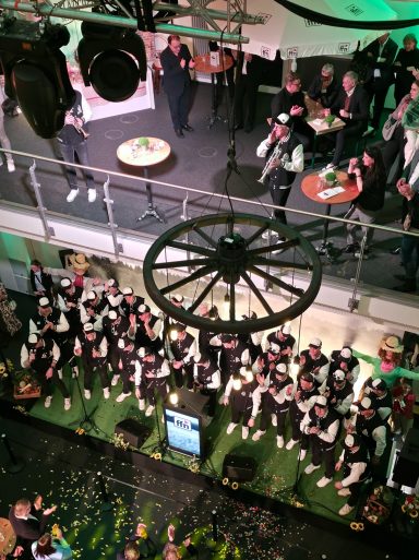 Eine Menschenmenge betrachtet eine Aufführung auf einer Bühne, mit festlicher Dekoration.