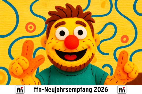 Bunte Figur mit roter Nase und fröhlichem Gesicht, lächelt und zeigt Peace-Zeichen.