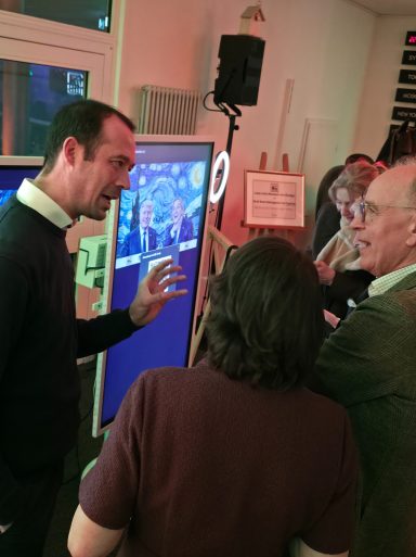 Mann erklärt interaktive Inhalte an einem Bildschirm, während andere aufmerksam zuhören.